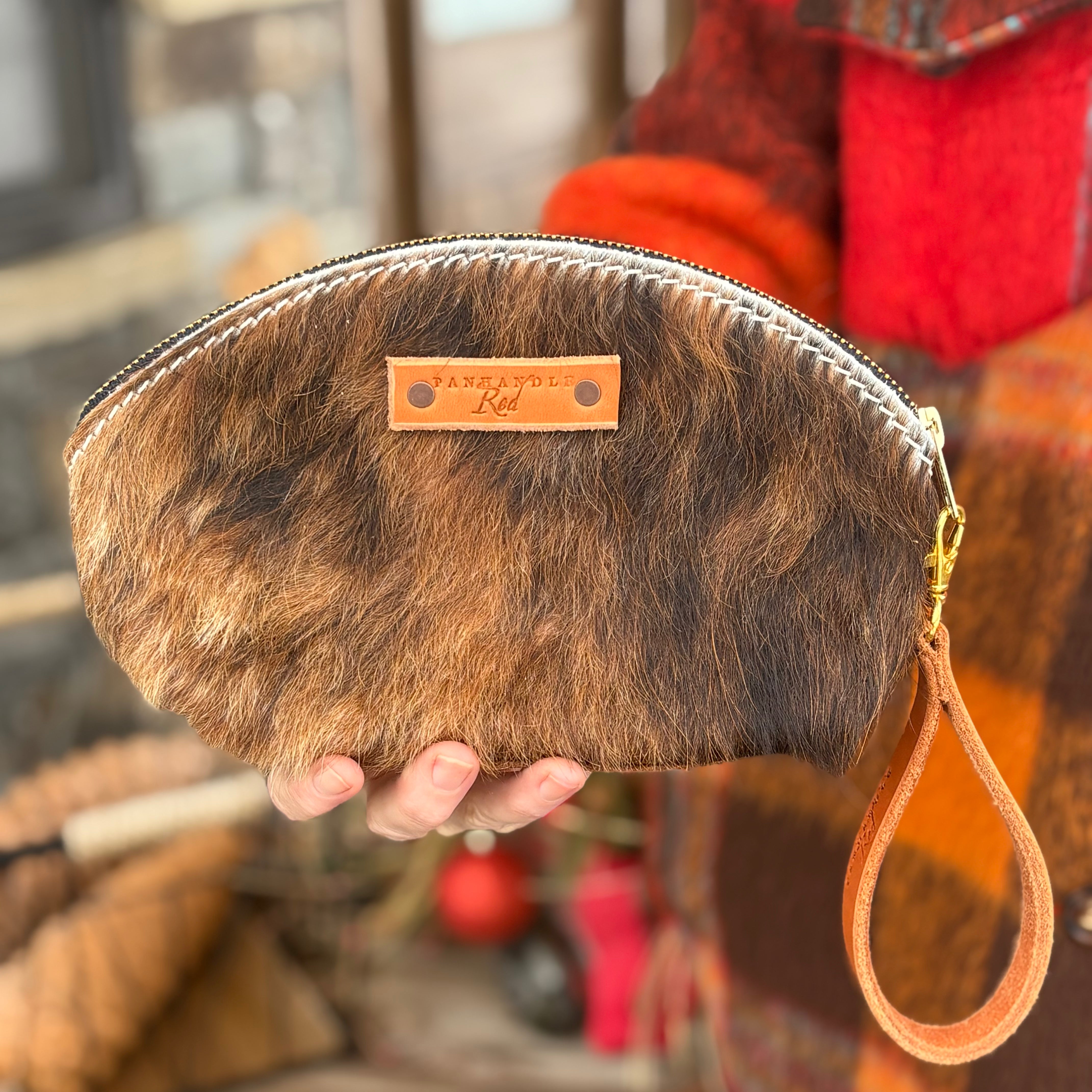Brown fur clutch with a visible brand logo held by a hand against a blurred background.