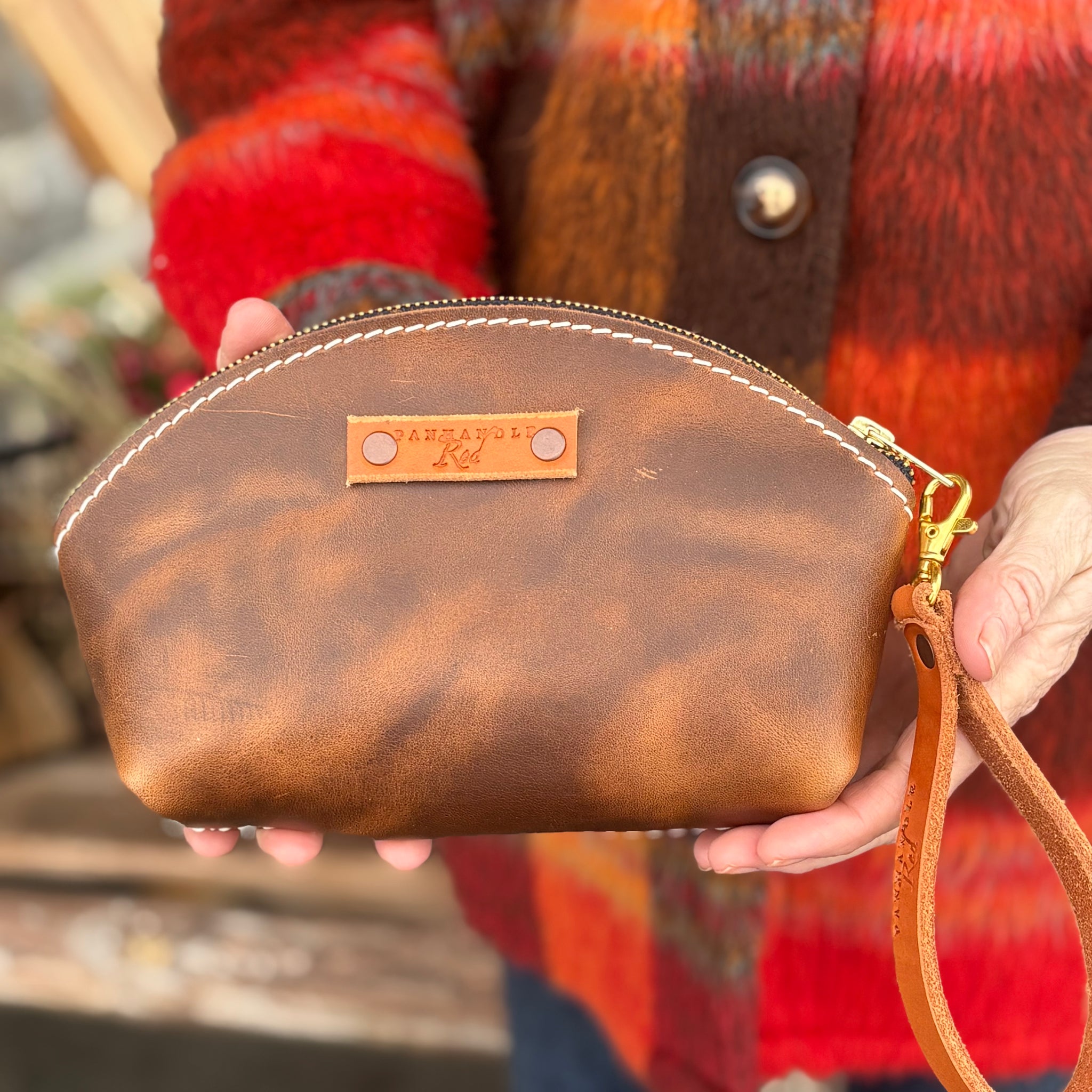 Brown leather clutch held by a person wearing a colorful plaid jacket.
